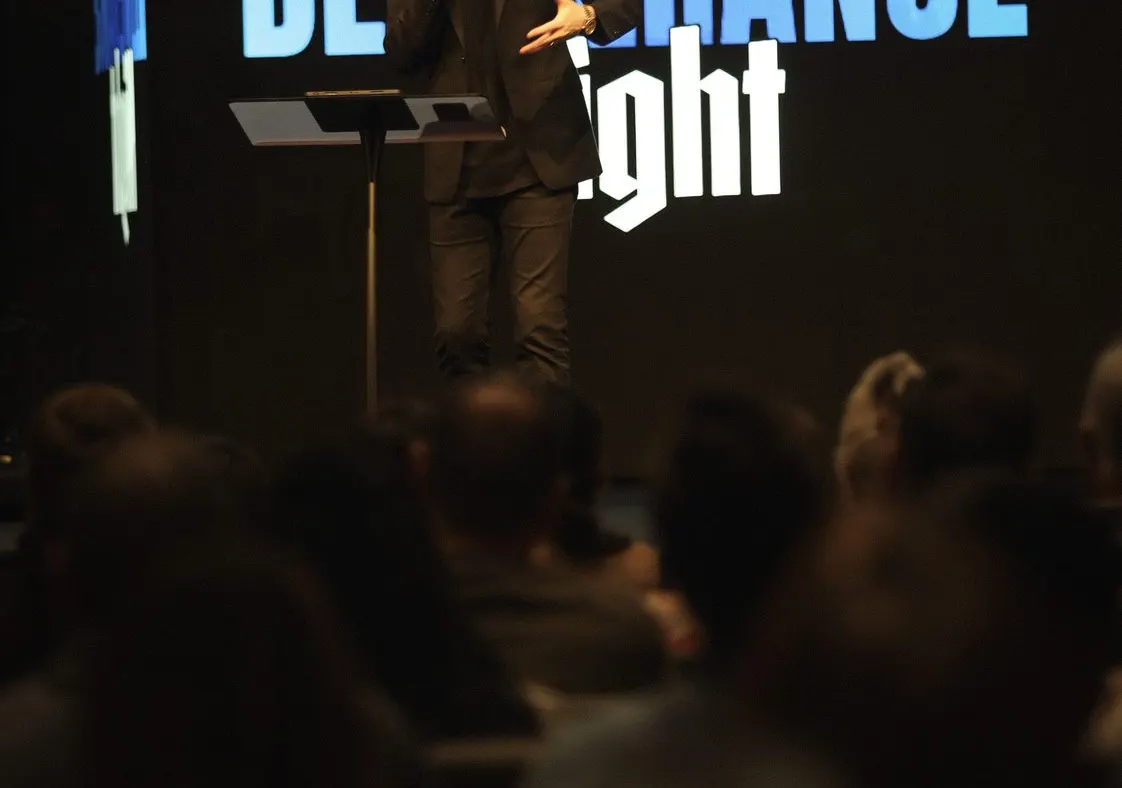 Alex Meadows preaching at a lectern before a seated audience, with Healing & Deliverance Night on the screen behind him.